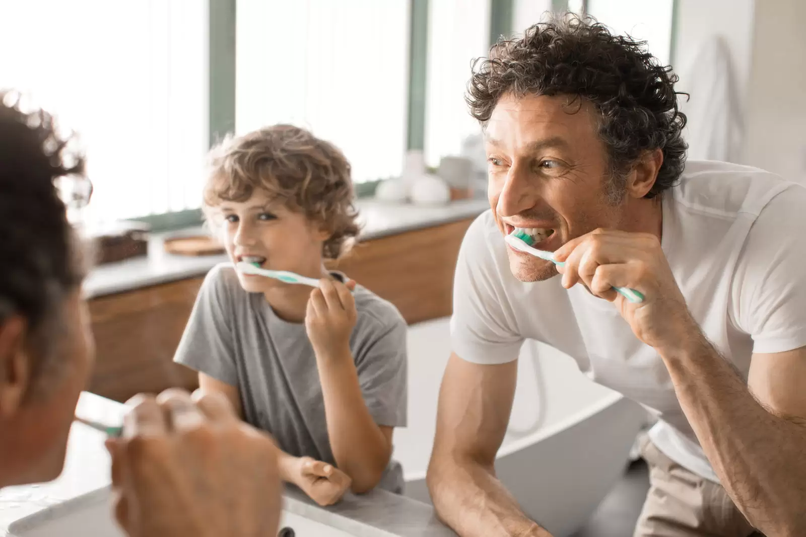 Vater und Sohn beim Zähneputzen sind mit Zahn-Zusatzversicherungen abgesichert.