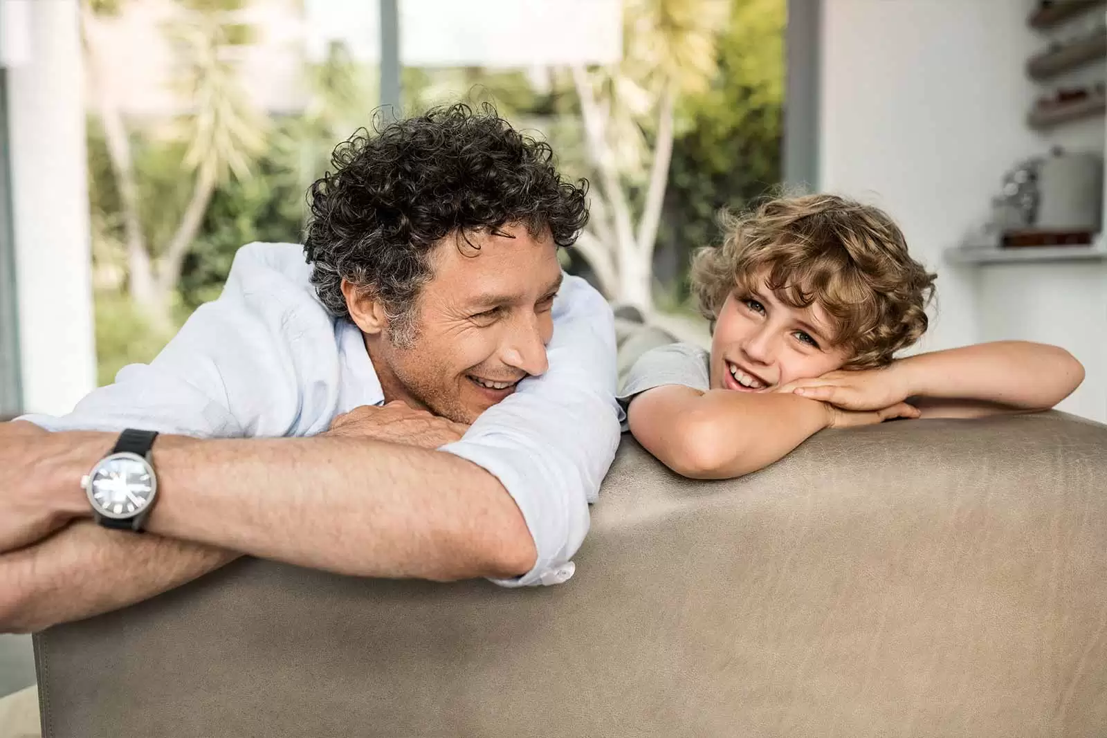 Vater und Sohn entspannt auf dem Sofa dank Privat-Haftpflichtversicherung