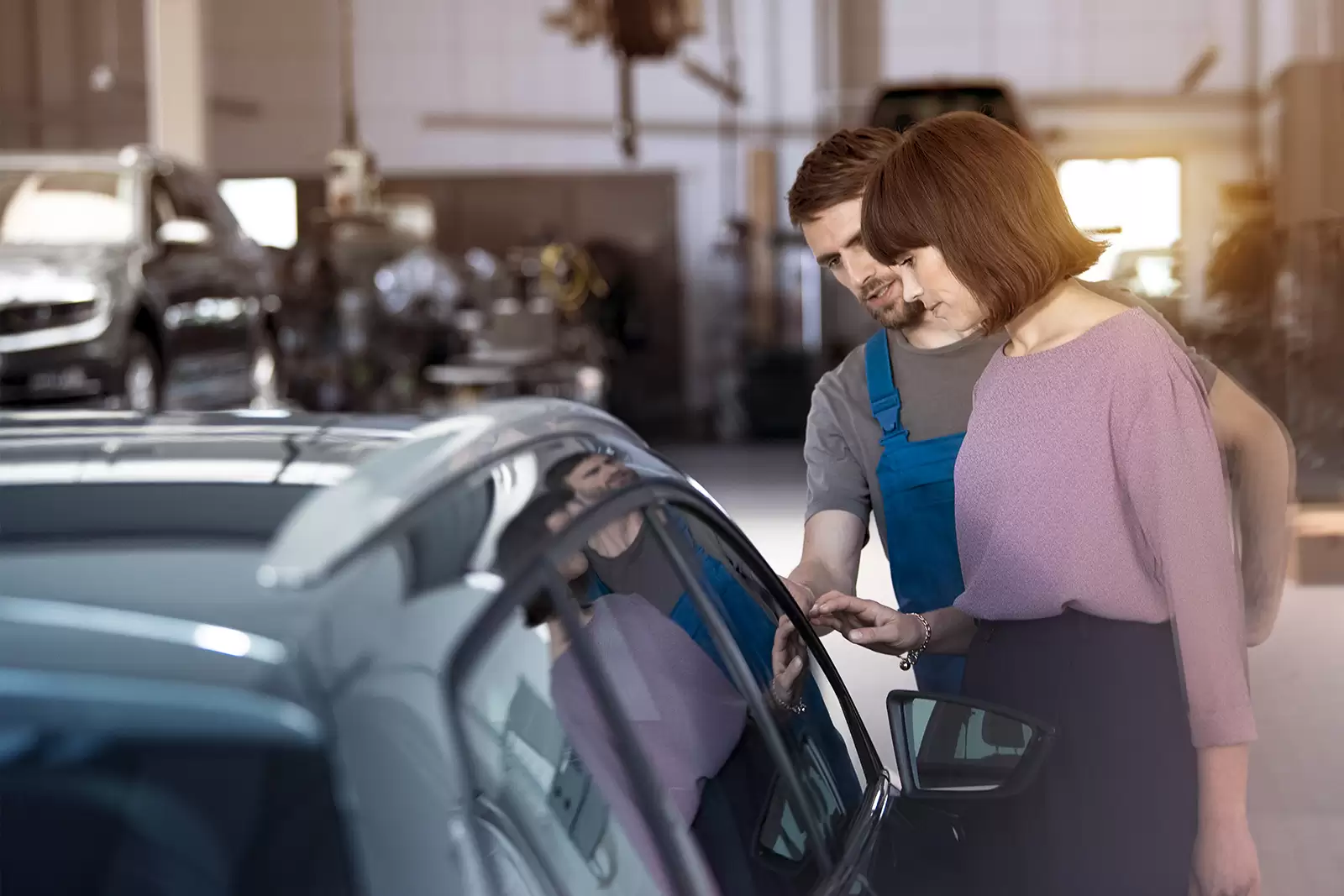 Frau und Mechaniker schauen sich in der Werkstatt ein Auto an