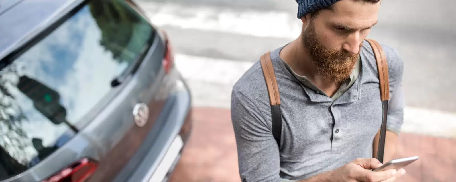 Ein Mann steht mit seinem Smartphone vor einem Auto.