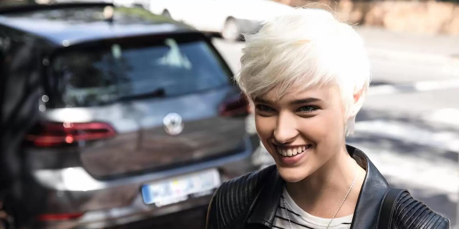 Eine blonde Frau mit einem Handy vor einem grauen Auto