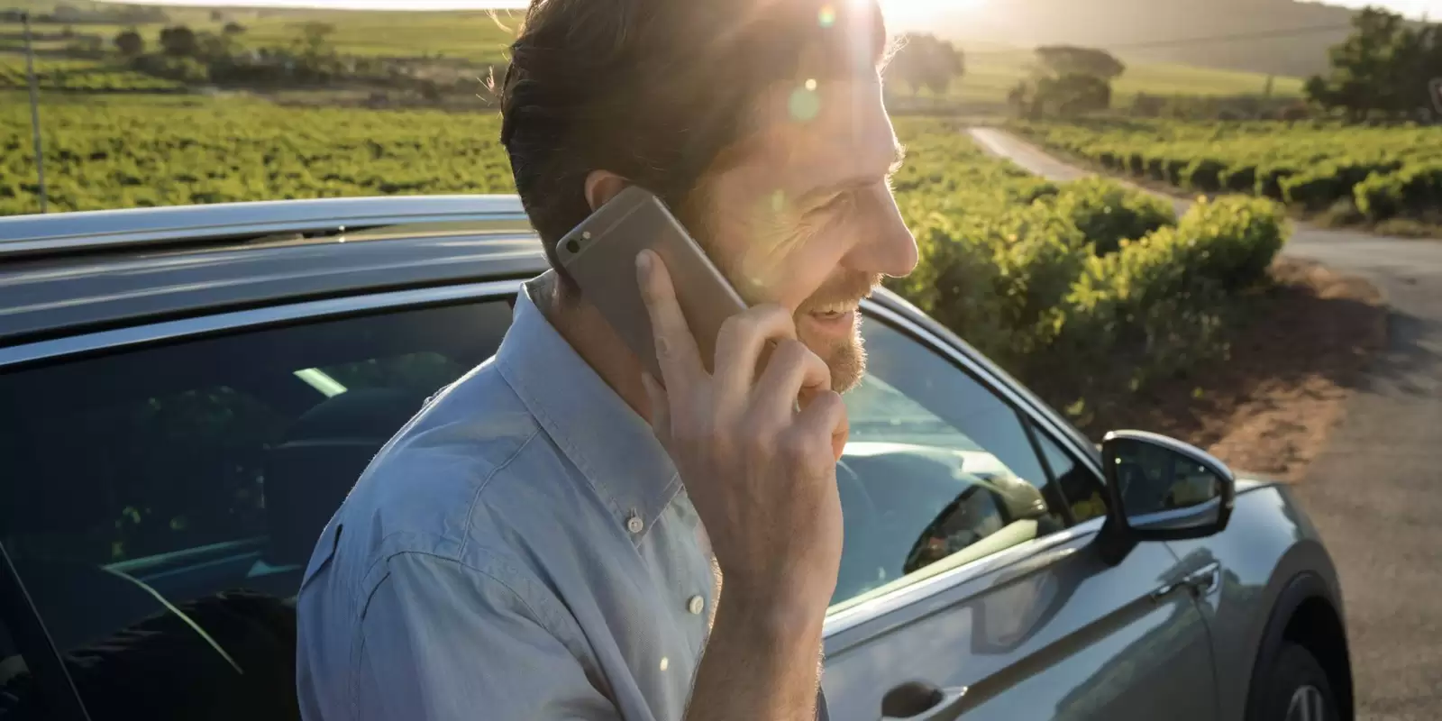 Ein Mann lehnt an einem dunklen Auto, während er mit einem Smarpthone telefoniert.