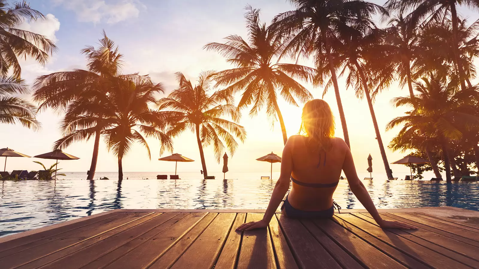 Frau sitzt im Sonnenuntergang am Wasser mit Palmen