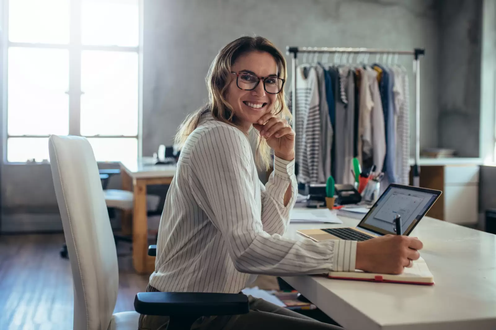 Eine Geschäftsfrau sitzt in ihrem Büro am Schreibtisch und lächelt in die Kamera
