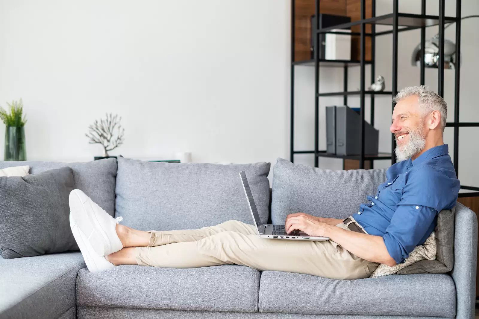 Ein Mann liegt entspannt mit einem Laptop auf dem Schoß auf dem Sofa.